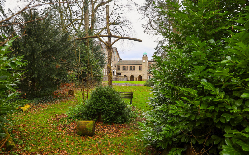 Image of a large wooden cross made of tree branches amongst hedges with a view through to the Cliff College building